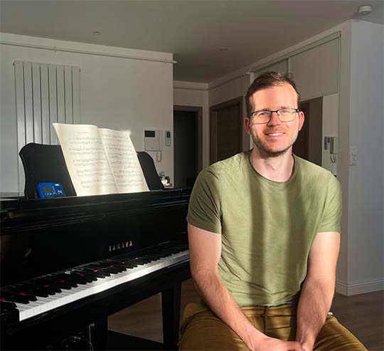 Alexandre souriant à côté de son piano, prêt à accueillir ses élèves